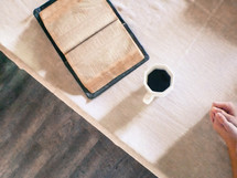 open Bible, coffee mug, and praying hands on a tablecloth 