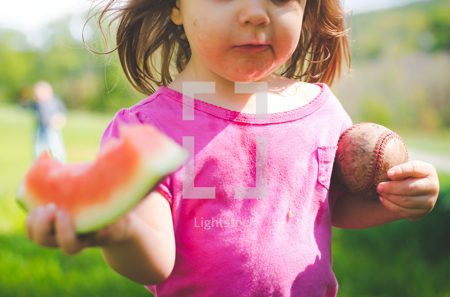a messy child holding a watermelon and ball 