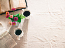 open Bible, flowers in a vase, and coffee mug on a tablecloth 