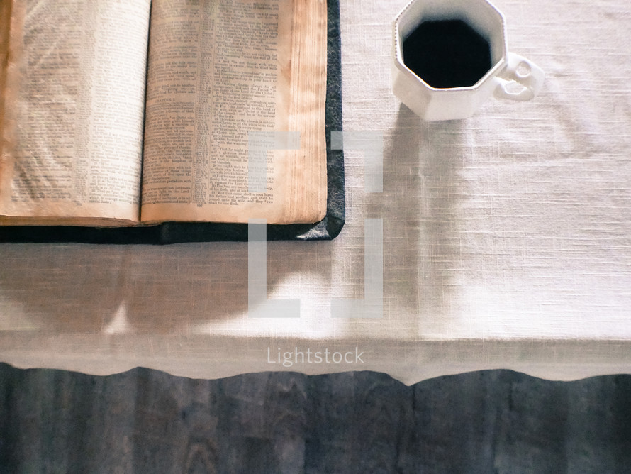 open Bible and coffee mug on a tablecloth 