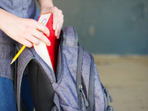 a student putting a book in a book bag 