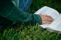 Hand on an open Bible in the grass.
