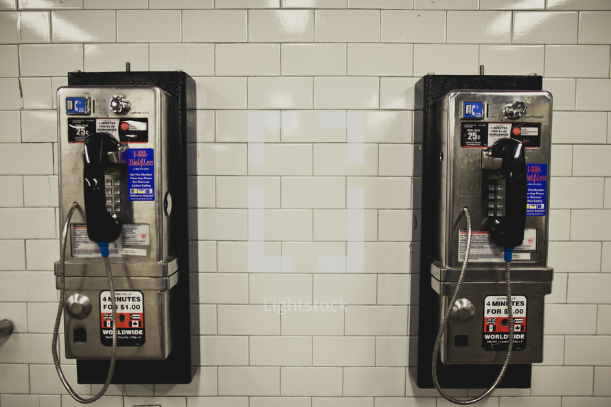 two modern pay phones on white tile wall