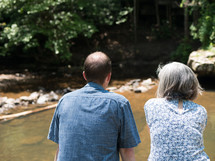 an elderly couple sitting and watching a river 