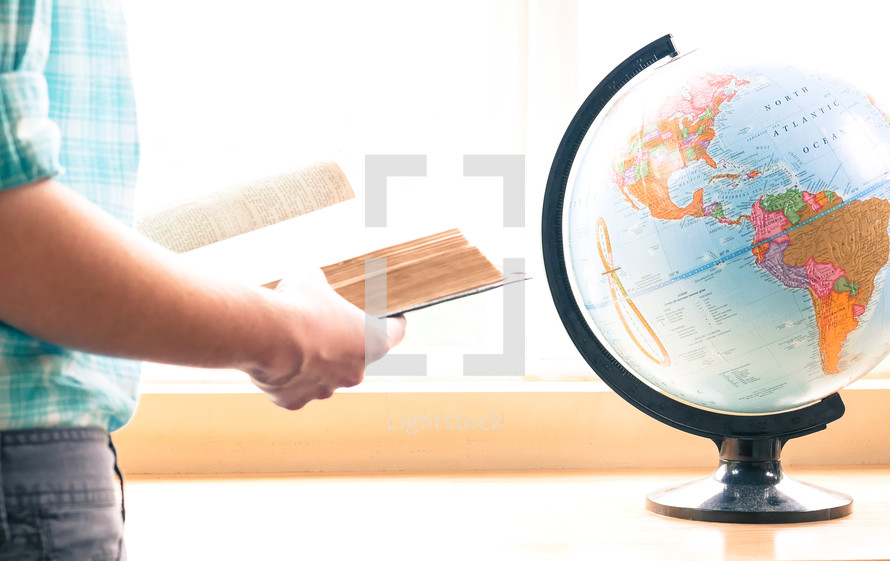 a teen girl standing and reading a Bible next to a globe 