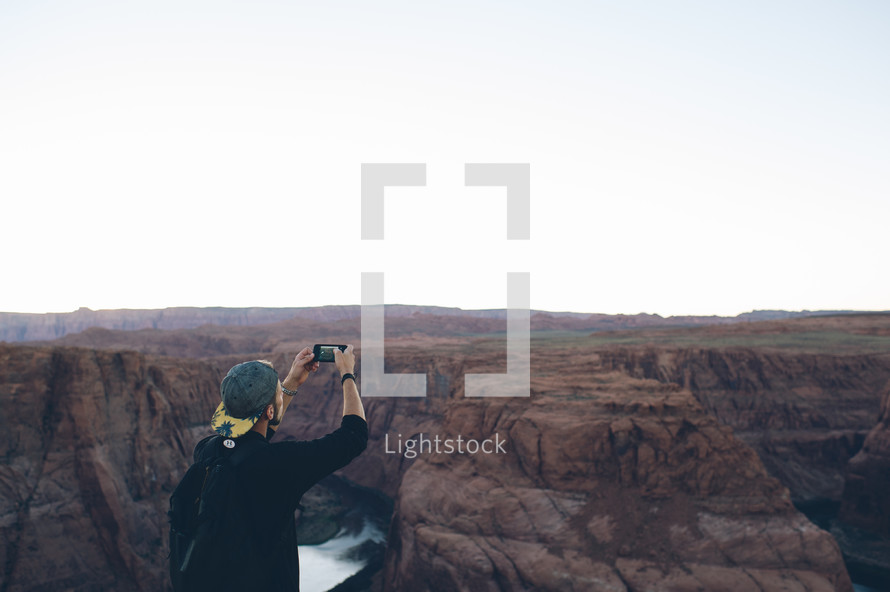 man taking a picture of a canyon with his cellphone 