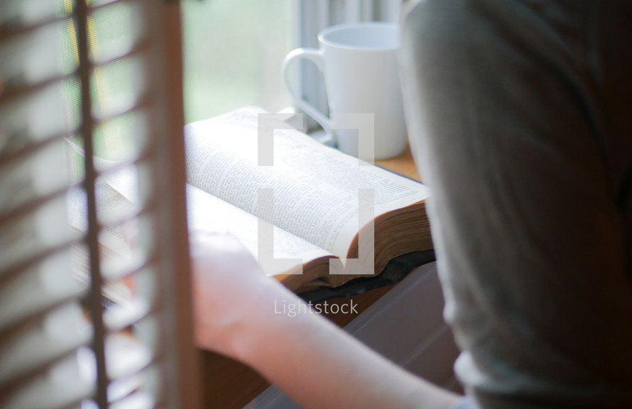 woman reading a Bible in a window seat at a cafe 