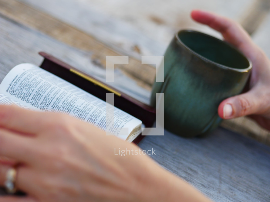 hand on a coffee mug while reading a pocket Bible 
