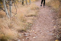 a woman walking on a dirt path through a fall forest 