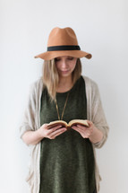 a woman in a hat standing reading a Bible 