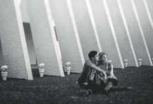 Couple sitting closely together on ground with modern building in background.