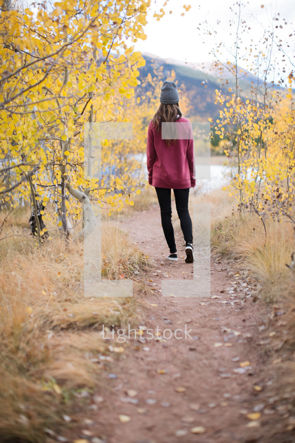 a woman walking down a dirt path towards a lake in fall 
