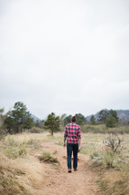 man in a plaid shirt walking on a path carrying a Bible 