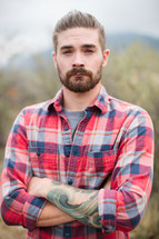 man in a plaid shirt with arms folded across his chest 