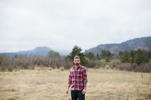 man in a plaid shirt standing outdoors in an open field 