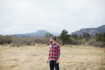 man in a plaid shirt standing outdoors in a field 