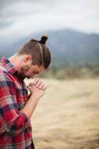 man in a plaid shirt with his head bowed in prayer 