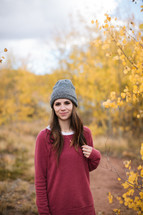 a woman in a wool cap standing in a fall forest 