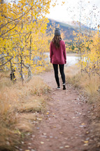a woman walking down a dirt path towards a lake in fall 