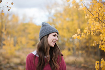 a woman in a beanie standing outdoors in a fall forest 