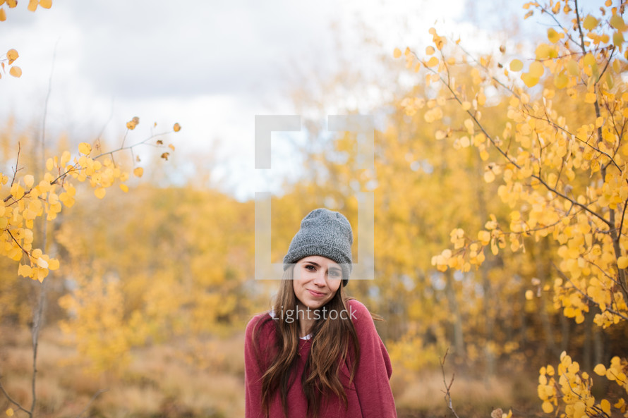 a woman in a wool cap standing in a fall forest 