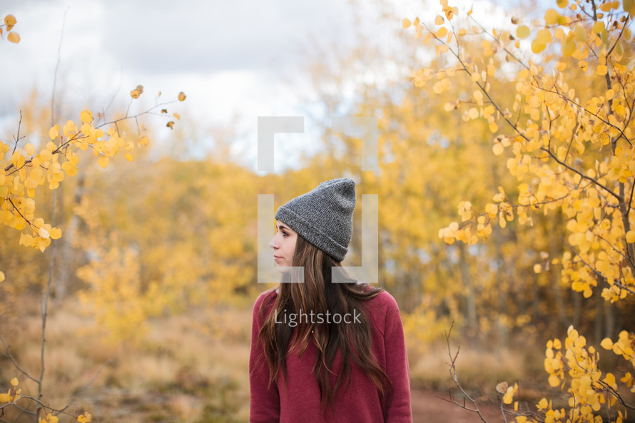 a woman in a wool cap standing in a forest in fall 