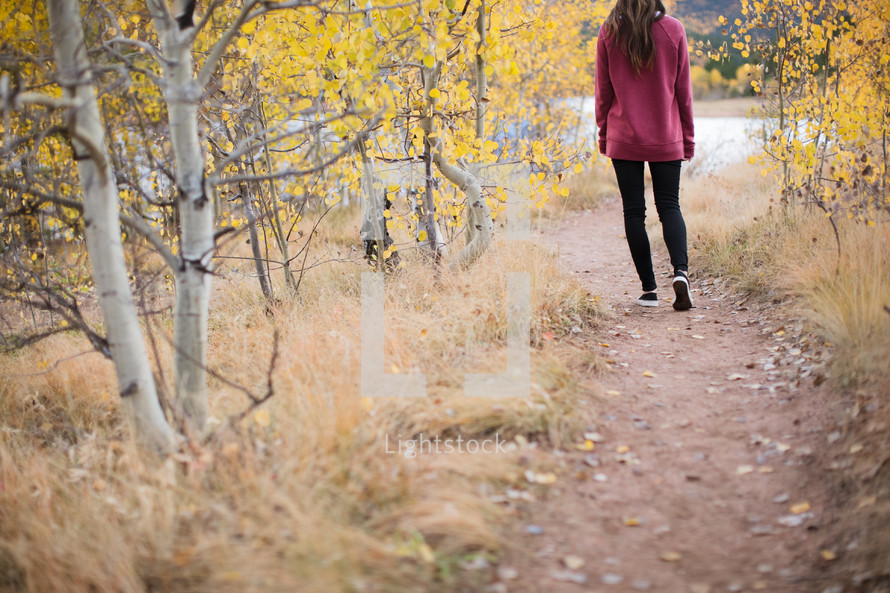 a woman walking down a dirt path in fall 
