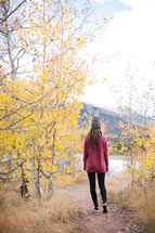 a woman walking on a dirt path towards a lake in fall 