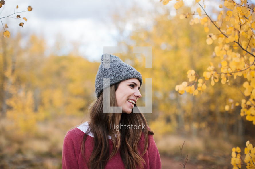 a woman in a beanie standing outdoors in a fall forest 