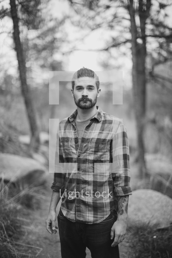 portrait of a man in a plaid shirt standing in a forest 