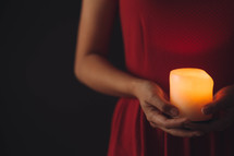 A woman in a red dress holds a lit candle.
