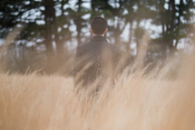 a man in a leather jacket walking through a field of tall grasses