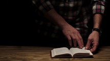 man standing turning the pages reading a Bible 
