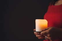 A woman holds a brightly burning candle.
