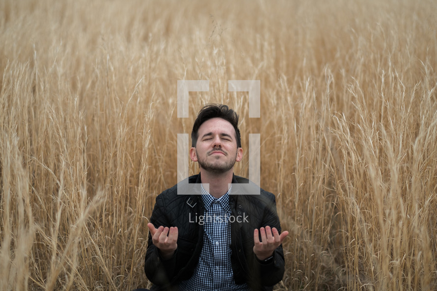 a man kneeling in tall grass in prayer