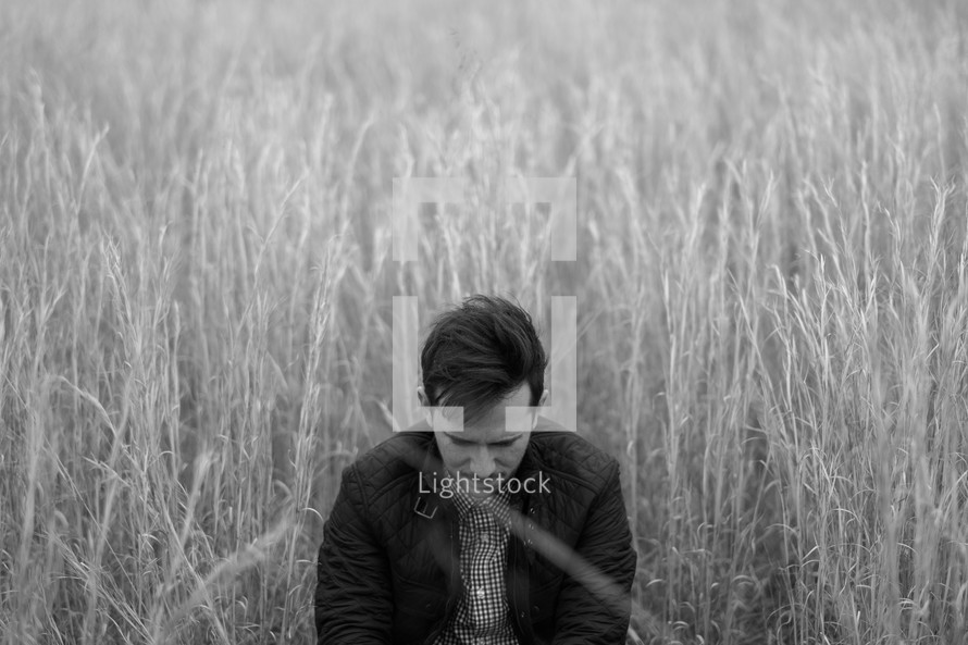 a man with head bowed in prayer in tall grasses 