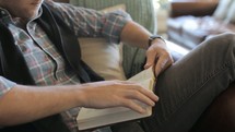 Man sitting on a couch relaxing and reading the Bible.