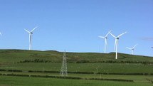 Moving wind turbines on a grassy hill by an oil well.