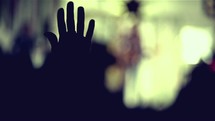 Silhouette of raised hand swaying in worship at a concert.