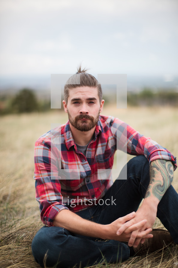 man in a plaid shirt siting on the ground 