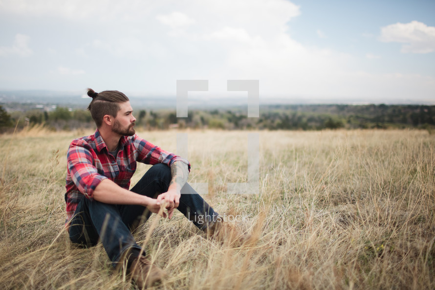 man in a plaid shirt sitting on the ground outdoors