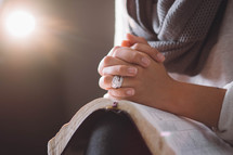 A woman sits with hands clasped on an open Bible.