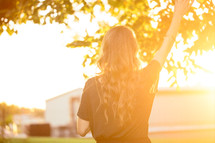 woman with her hand raised in worship standing outdoors under intense sunlight 