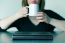woman drinking hot cocoa and Bible on a table 