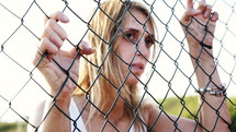 Woman holding onto a wire fence with a serious look on her face.