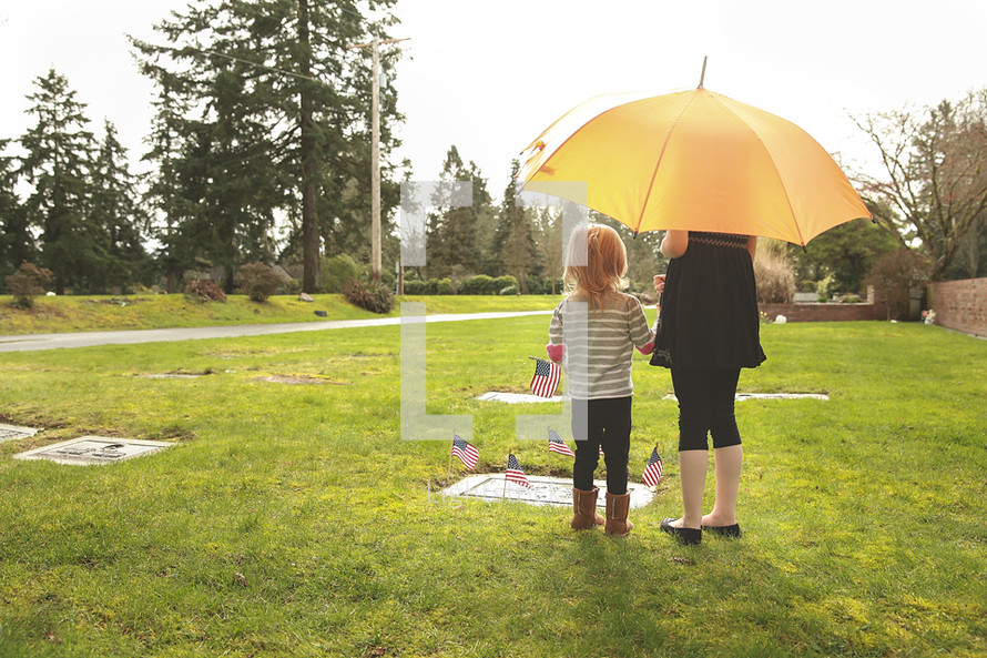A woman and child stand under an umbrella at the grave of a soldier.