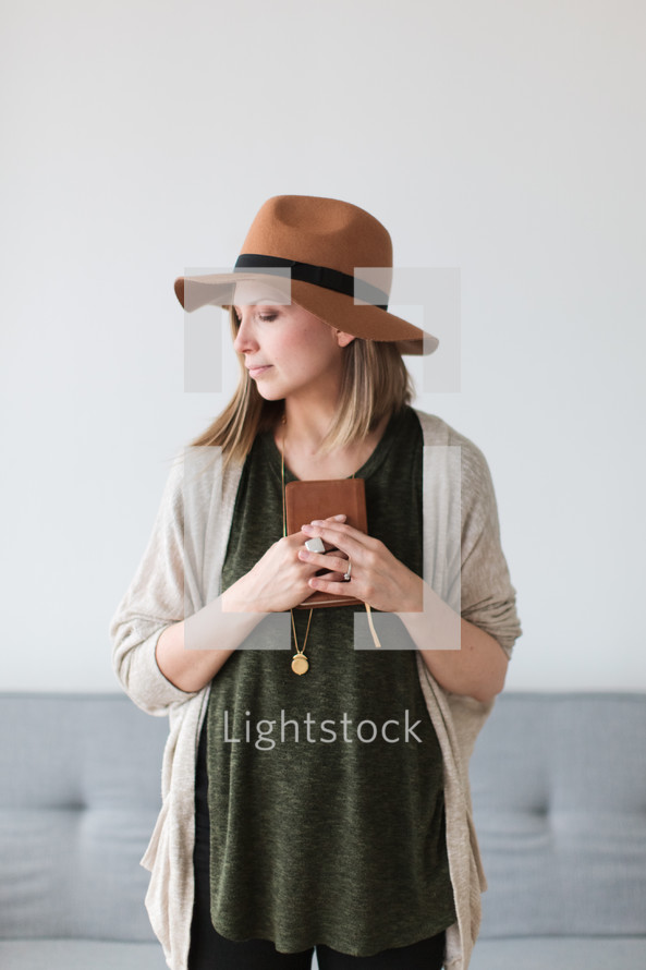 a woman in a hat holding a Bible close to her heart 