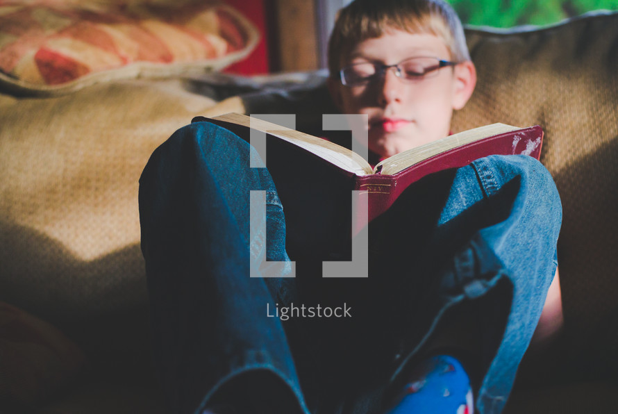 kid reading a Bible on a couch 