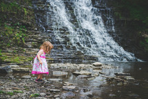 a girl playing with rocks by a stream 