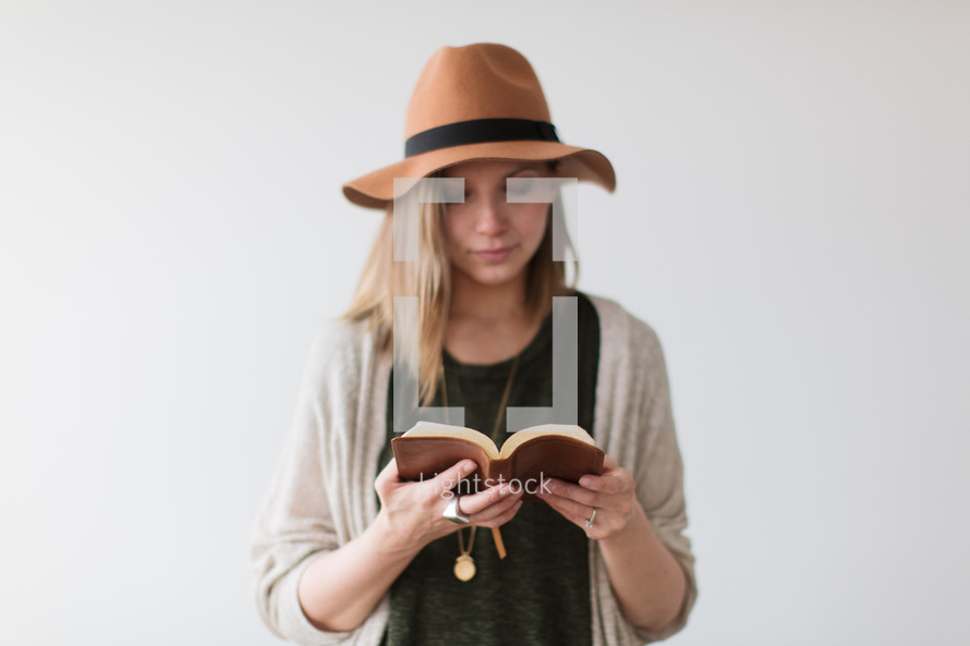 a woman in a hat standing reading a Bible 